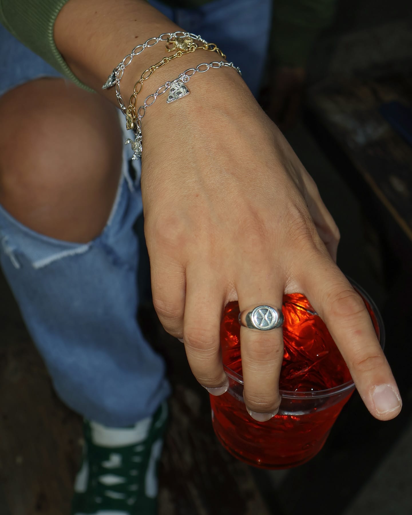 Charm bracelets and a signet ring from the jewellery collaboration, hand resting on a Negroni