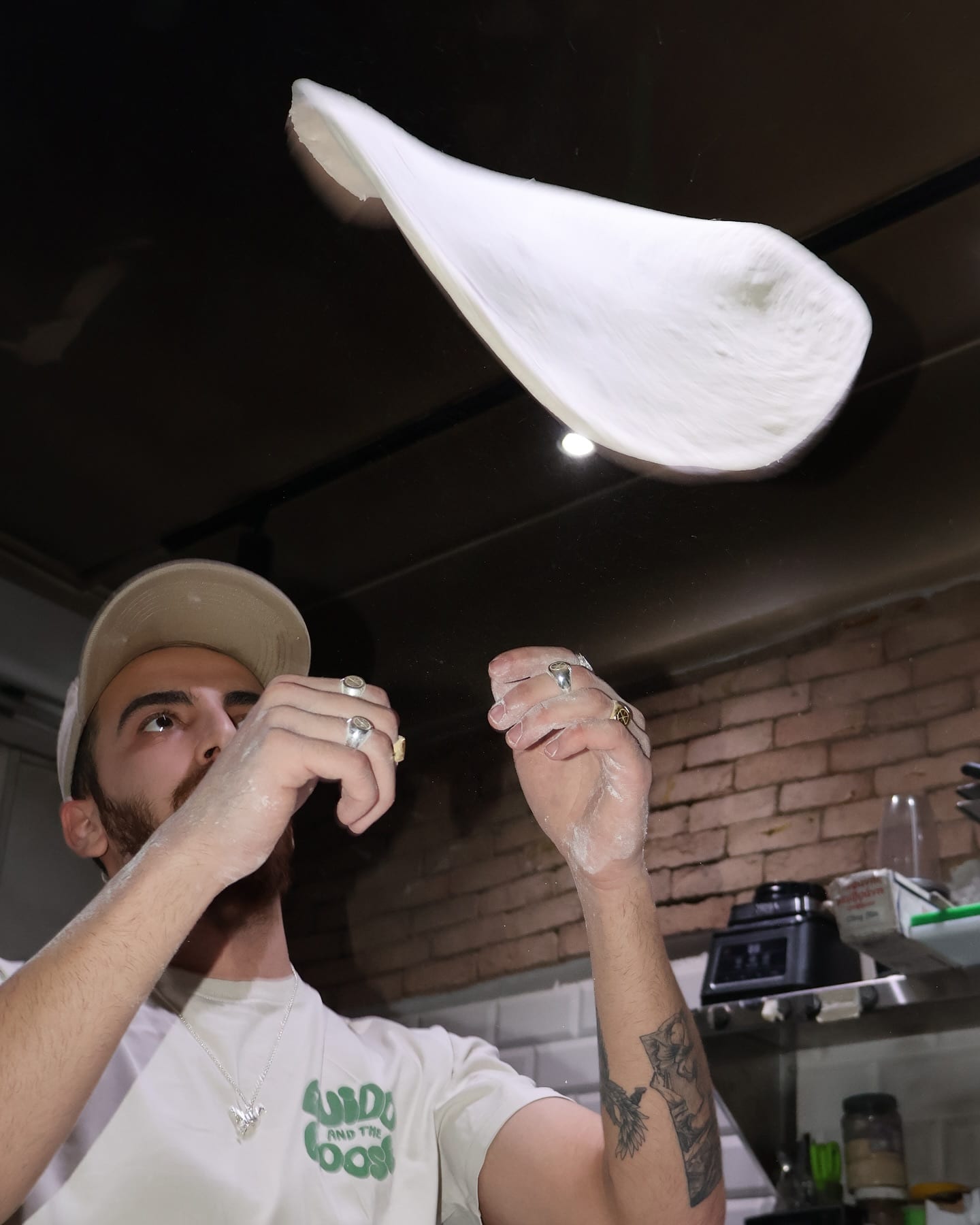 Pizzaiolo in a Guido & The Goose t-shirt tossing dough in the air
