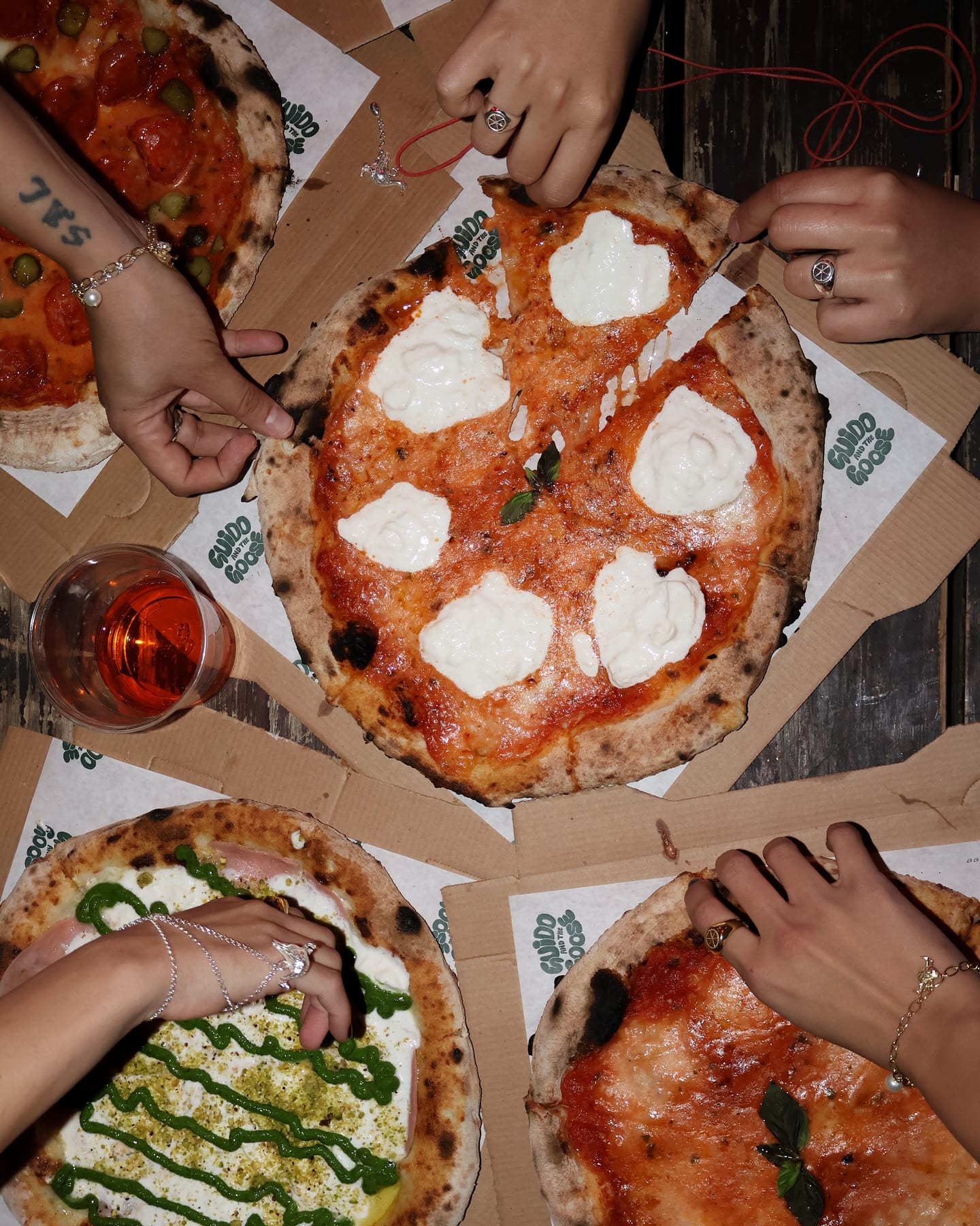 A table covered in Guido & The Goose pizzas, boxes and drinks, shot from above